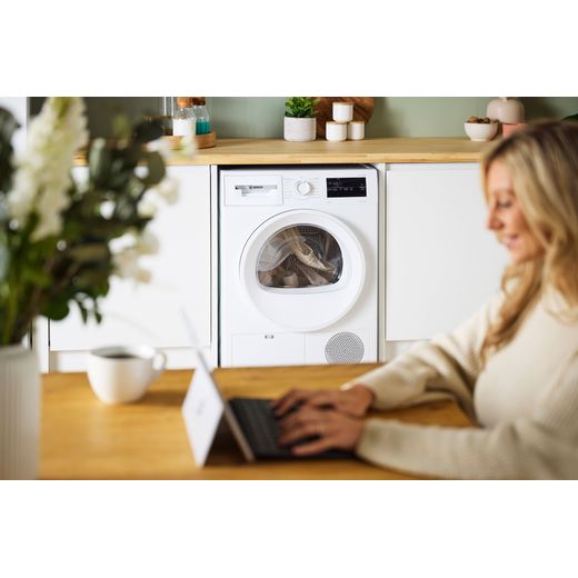 Bosch Series 4 WTH85225GB 8Kg Heat Pump Tumble Dryer - White - Women using laptop on table shot