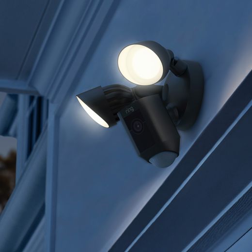 Ring Floodlight Cam Wired Plus Full HD 1080p Smart Home Security Camera - Black - Camera on wall at nights with lights on shot