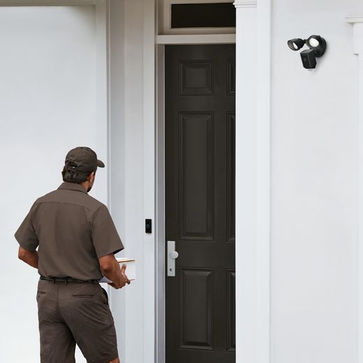 Ring Floodlight Cam Wired Plus Full HD 1080p Smart Home Security Camera - Black - Man walking to door with camera on wall shot