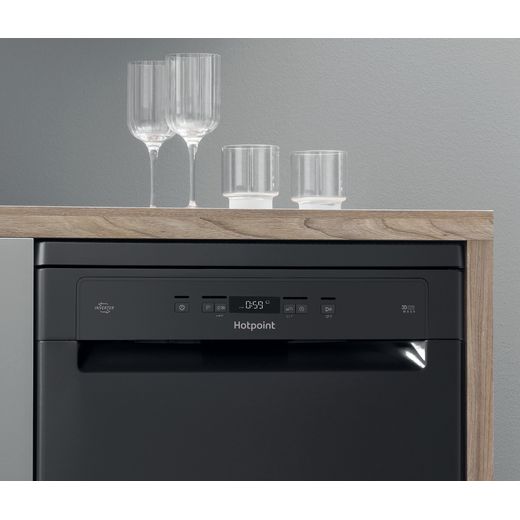 Hotpoint Standard Dishwasher - Black - Closeup of top quarter of dishwasher under a wooden worktop with glasses on it