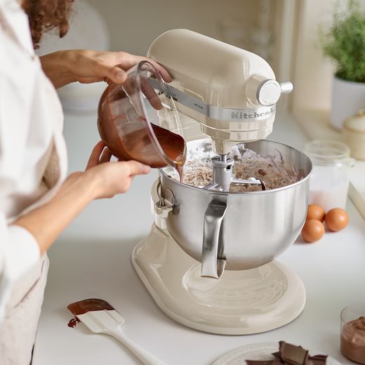 KitchenAid Artisan 5KSM60SPXBAC Stand Mixer with 5.6 Litre Bowl - Almond Cream - Woman pouring melted chocolate into mixer bowl