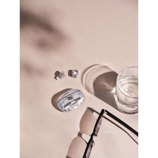 Beats Studio Buds + True Wireless Noise Cancelling In-Ear Headphones - Transparent - Headphones and couch on table next to glass of water