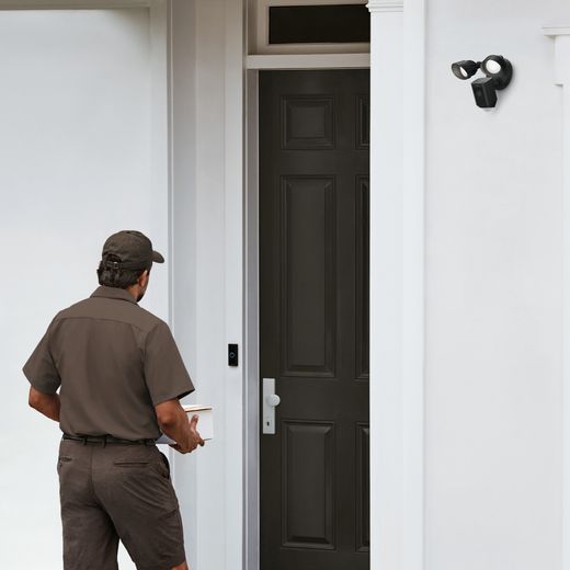 Ring Floodlight Cam Wired Plus Full HD 1080p Smart Home Security Camera - Black - Man walking up to door with camera on wall shot